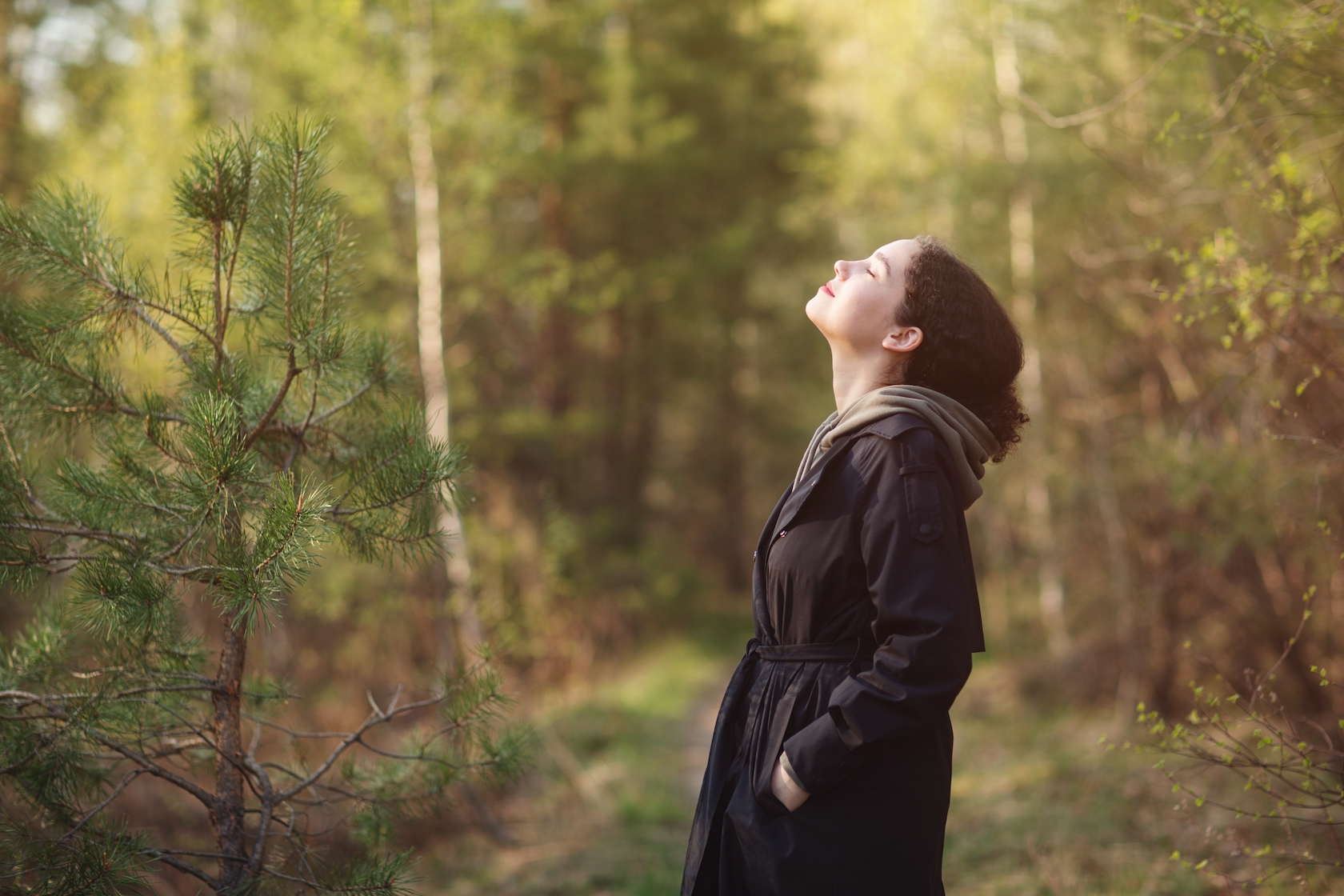 Leende kvinna blundar och andas frisk luft ute i solskenet i skogen.