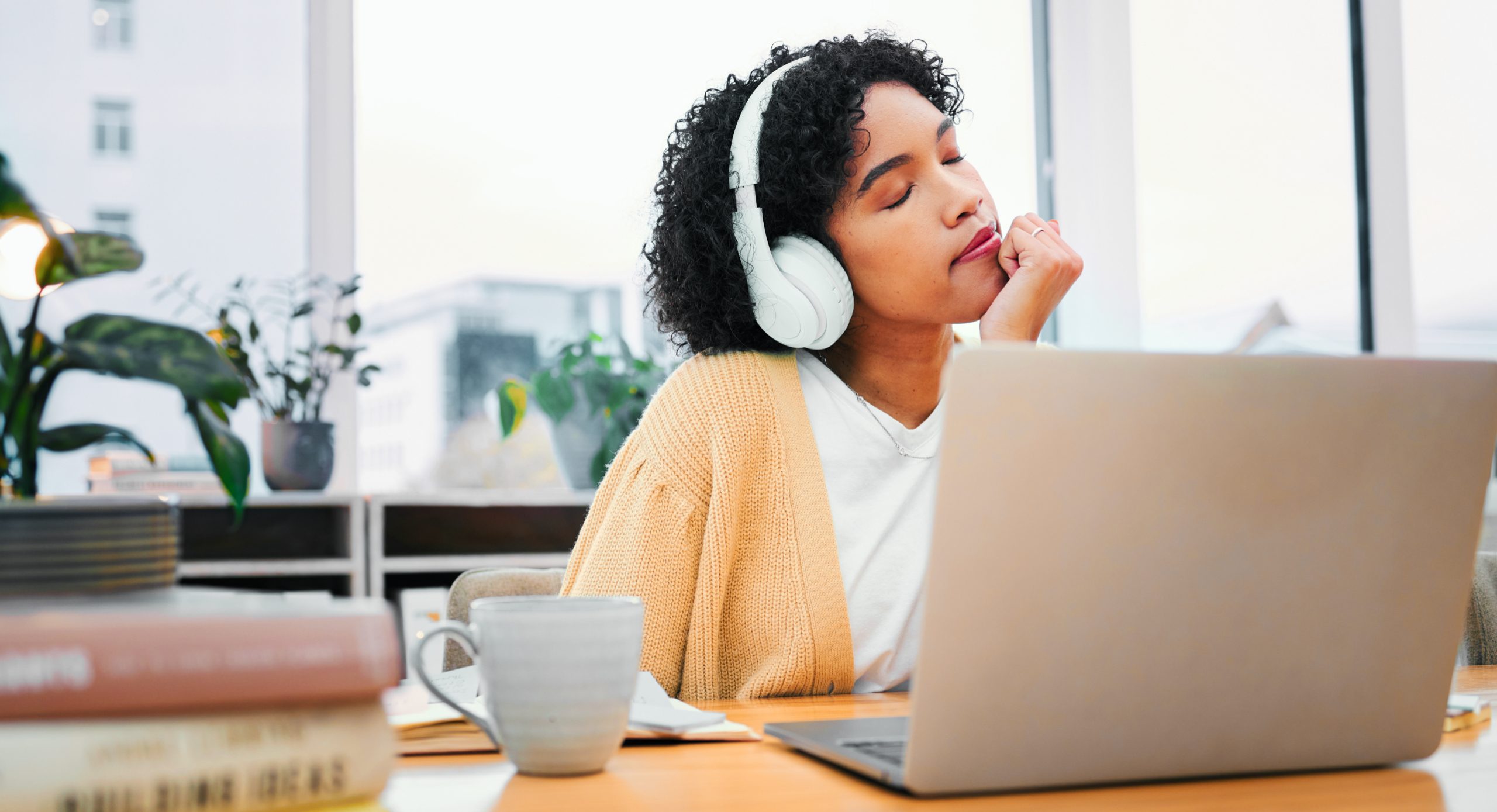 Calm woman sitting at a desk in a bright office with closed eyes earing headphones.